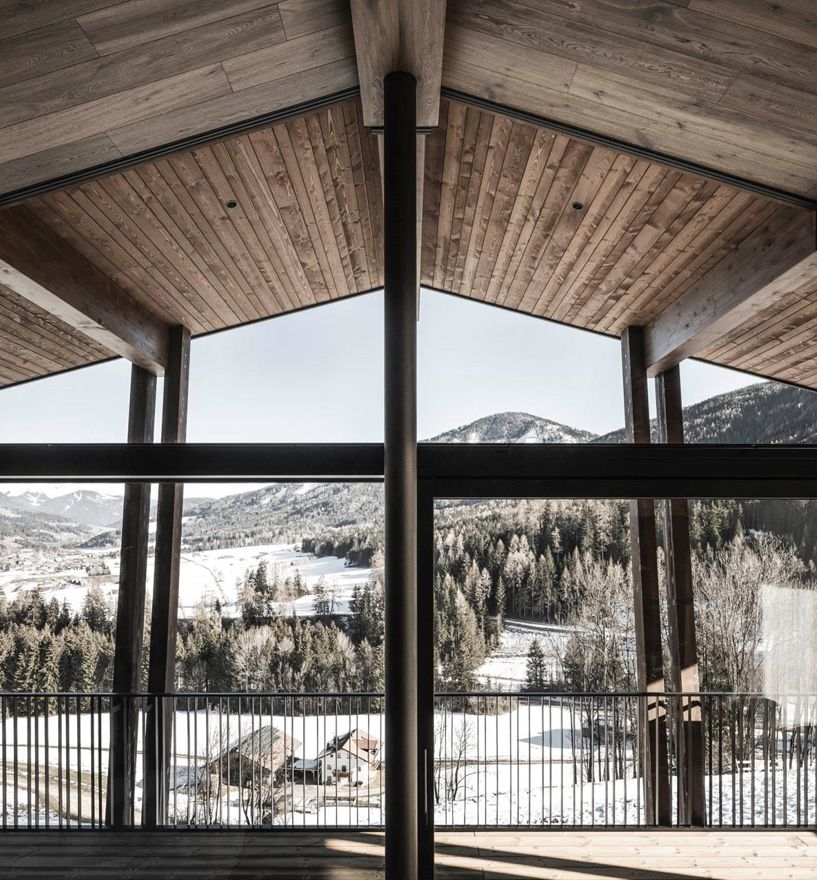 Große Fensterfront mit Holzdach, Blick auf verschneite Landschaft und bewaldete Berge.