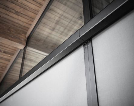 Detailansicht moderner Fassade mit schwarzem Rahmen und Sonnenschutzpanel.