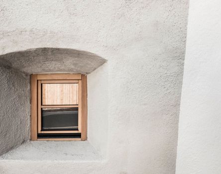 Kleines Fenster mit Holzrahmen in dicker, heller Steinwand